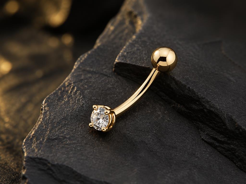 Gold curved navel barbell with a clear gem resting on dark stone
